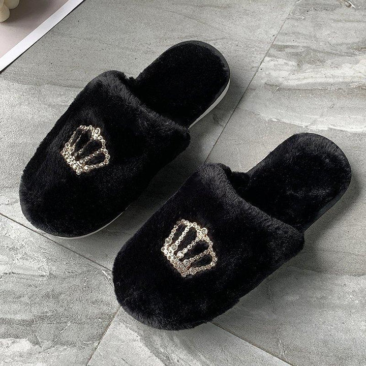 Black fuzzy slippers with golden sequin crown design on gray tile floor