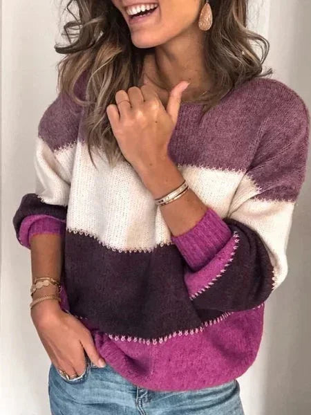 Woman wearing a cozy colorblock knit sweater with mauve, white, dark brown, and magenta stripes and blue jeans