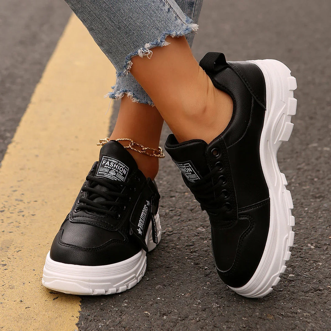 Black chunky sneakers with white soles worn with frayed denim jeans on asphalt road