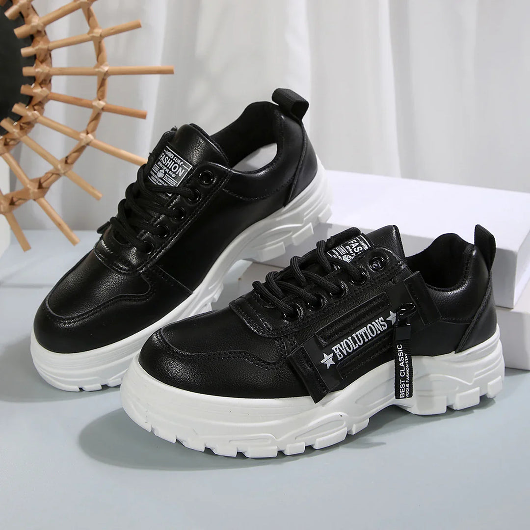 Black chunky sneakers with white soles and zip detail labeled Evolutions on gray surface