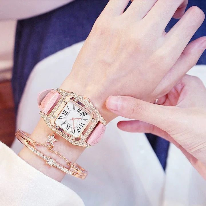 Woman's wrist with pink leather strap wristwatch featuring Roman numerals and gold tone crystal accents, paired with gold and crystal bracelets