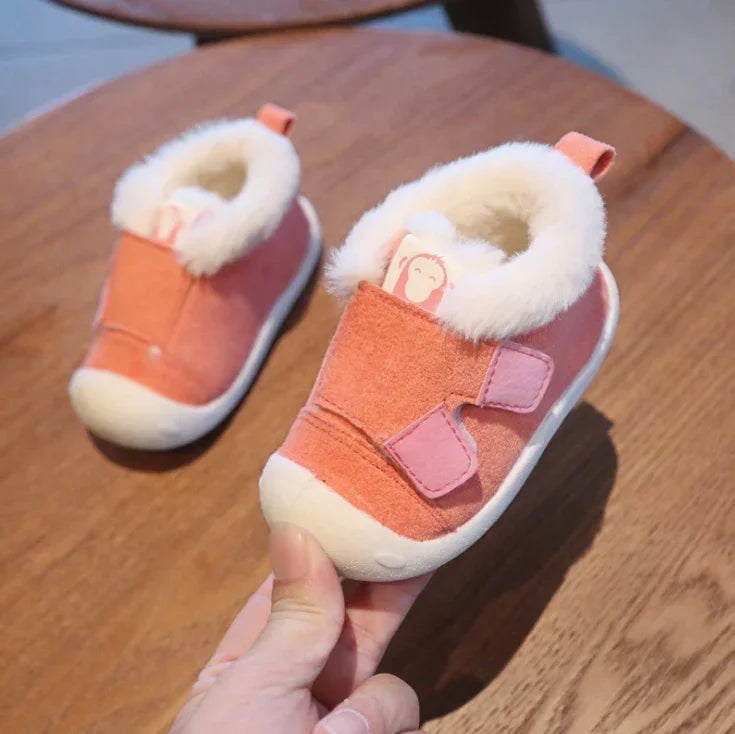Pink toddler winter shoes with white fur lining and soft soles on wooden table