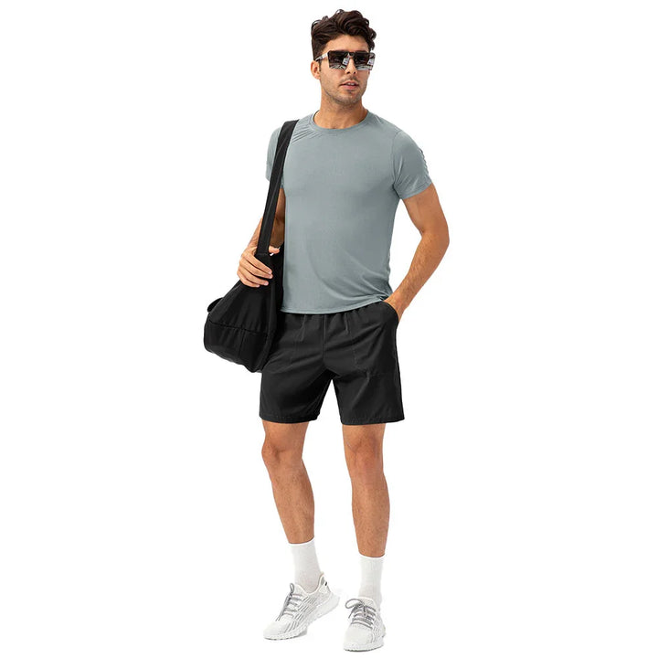 Man in athletic outfit with sunglasses, gray t-shirt, black shorts, gym bag, and white sneakers