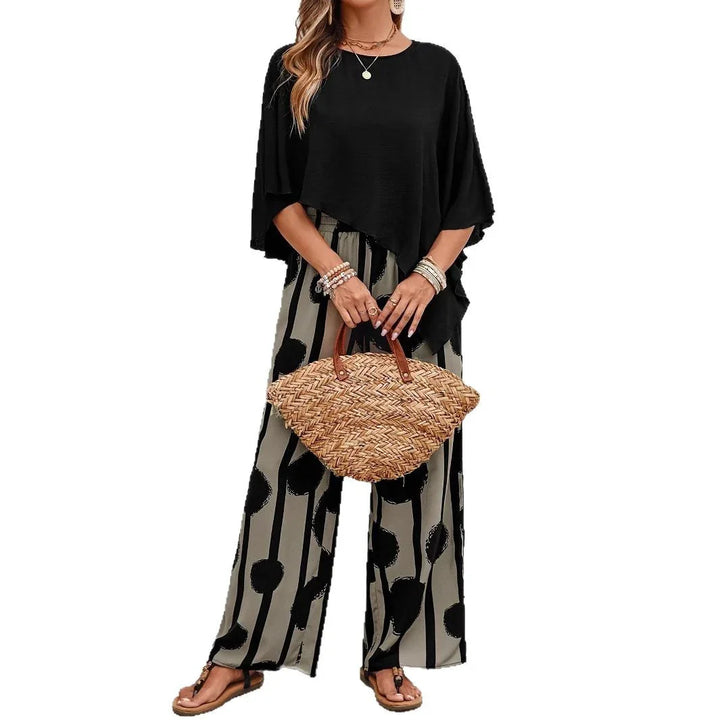 woman wearing black asymmetric top and patterned wide-leg pants holding woven straw handbag