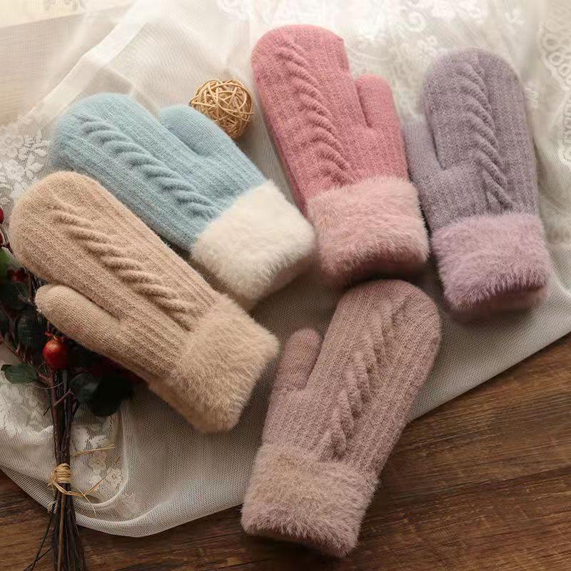 Five pairs of soft knitted winter mittens in pastel colors with fluffy cuffs on lace and wooden background