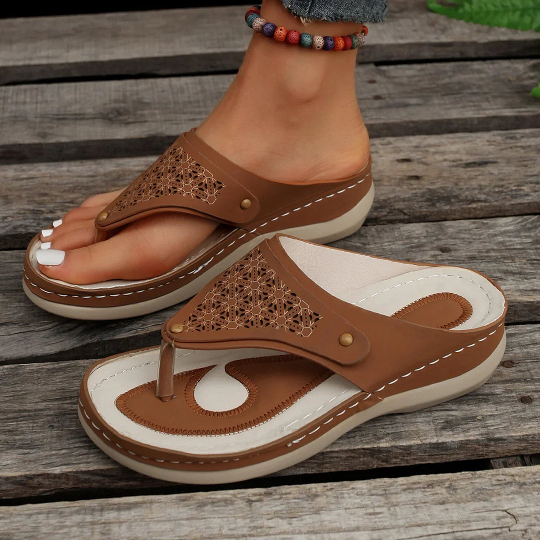 Brown leather women's thong sandals with cushioned white insoles on wooden floor, colorful anklet