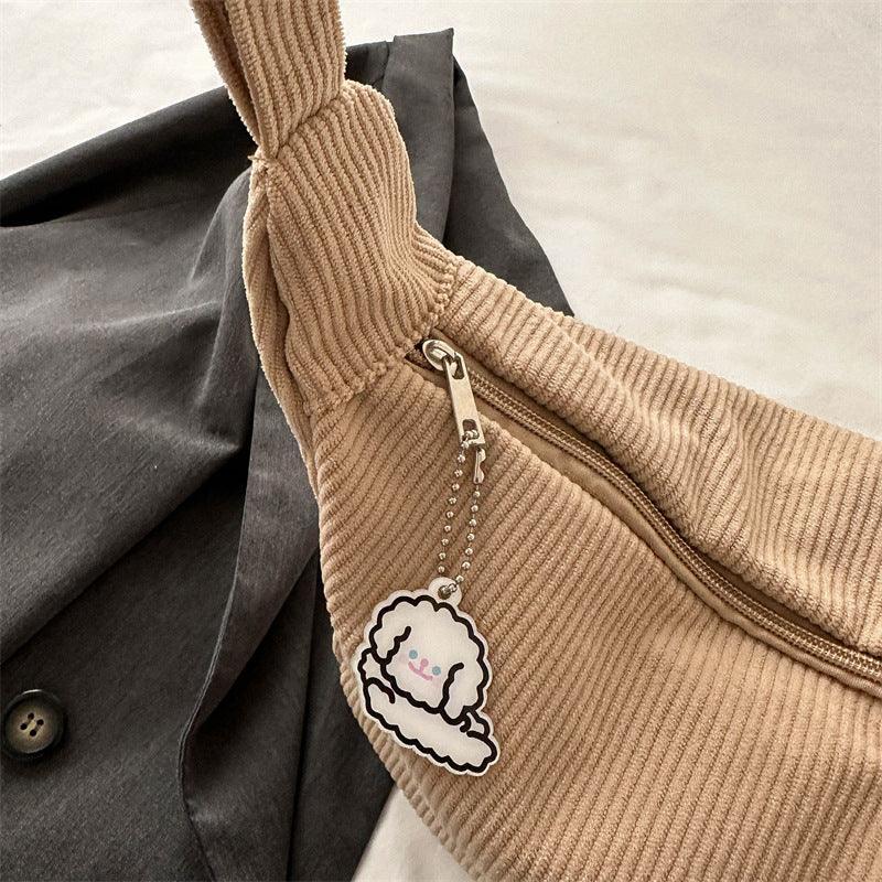 Beige corduroy shoulder bag with zipper and cute white dog keychain on dark gray fabric background
