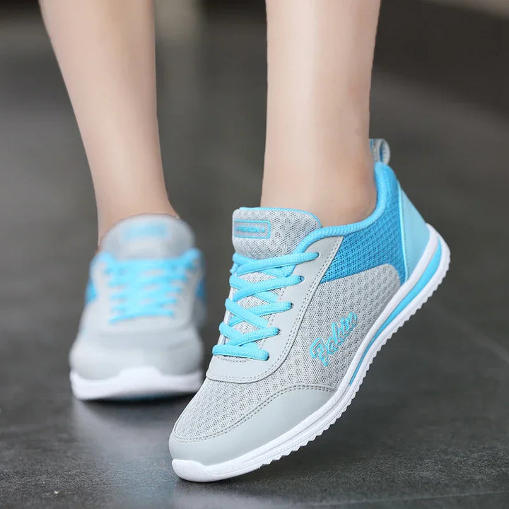Light gray and blue athletic sneakers with mesh fabric and laces worn on feet on a dark floor