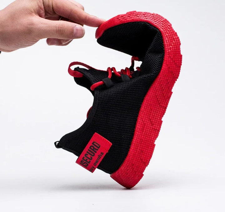 Black mesh sneaker with flexible red sole and red laces held by hand showing bendability