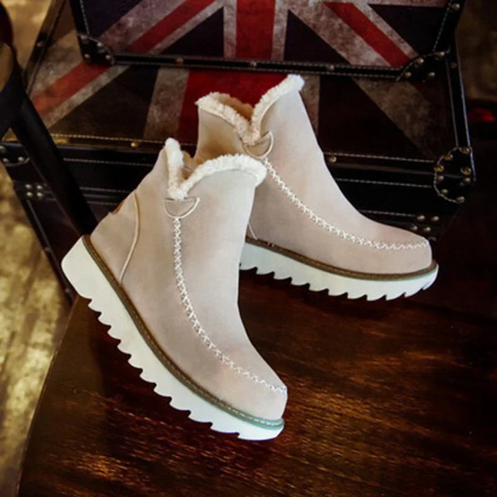 Beige winter boots with white fur lining and thick white soles on wooden surface with Union Jack trunk background