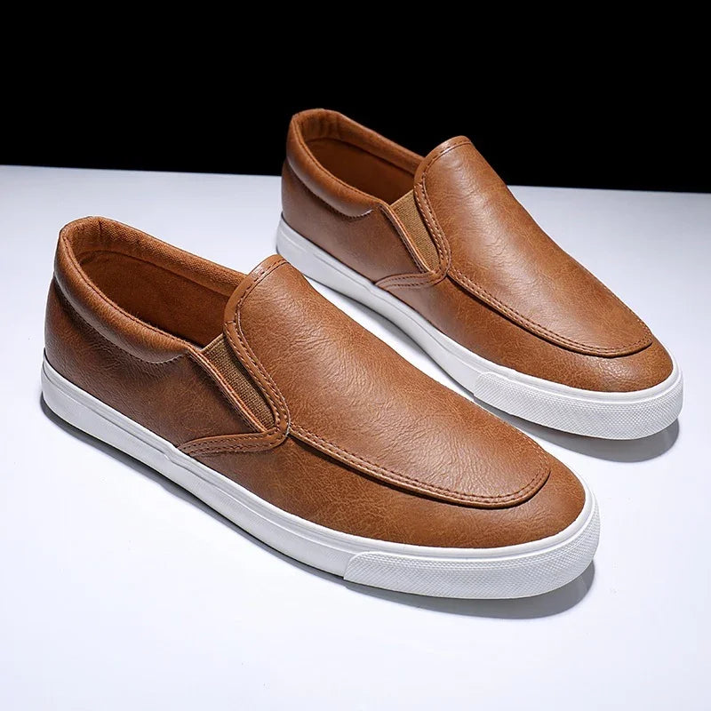 Pair of brown leather slip-on casual shoes with white rubber soles on white surface
