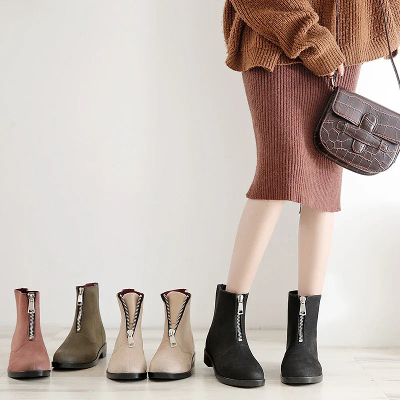 Woman wearing black front-zip ankle boots with brown knit skirt, holding textured brown handbag, and four other zipper boots in muted colors