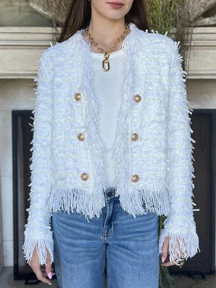 Woman wearing white textured fringe jacket with gold buttons, white top, gold chain necklace, and blue jeans