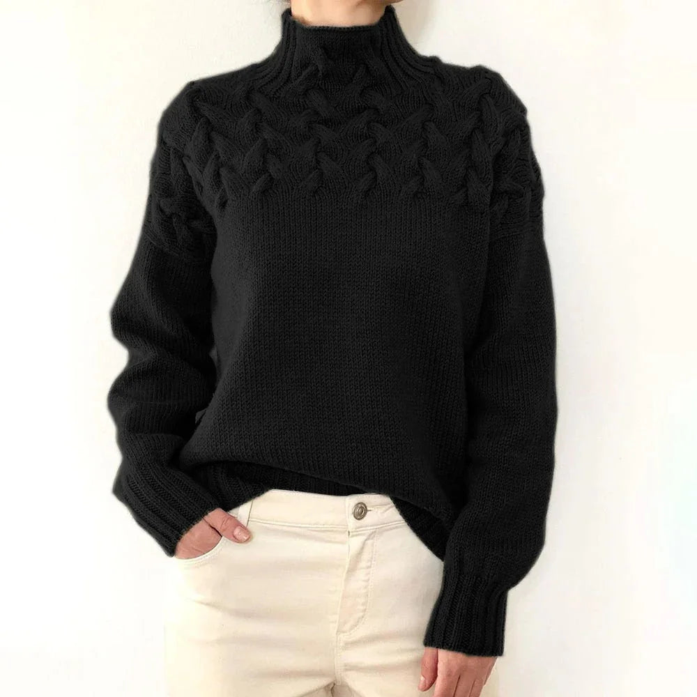Person wearing black cable knit turtleneck sweater with cream pants against white background