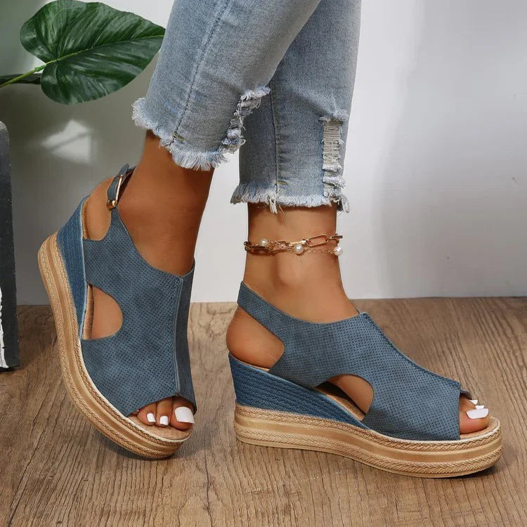 Blue wedge sandals with cutouts and ankle straps worn with distressed light blue jeans on wooden floor