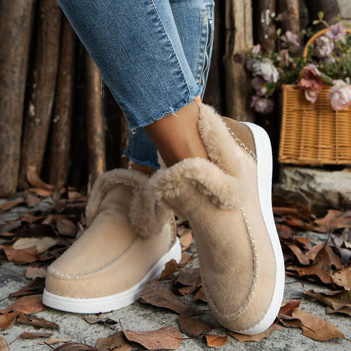 Women's beige fur-lined winter boots with white soles worn with blue jeans outdoors on fallen leaves
