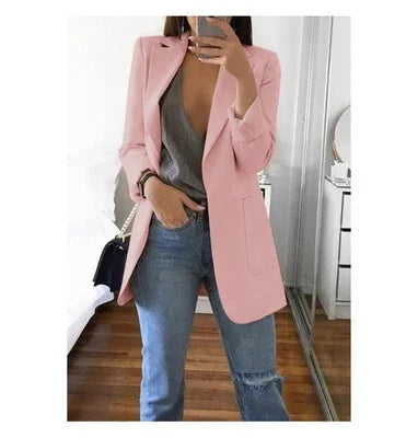 Woman wearing pink blazer over grey top and blue jeans taking mirror selfie in modern room