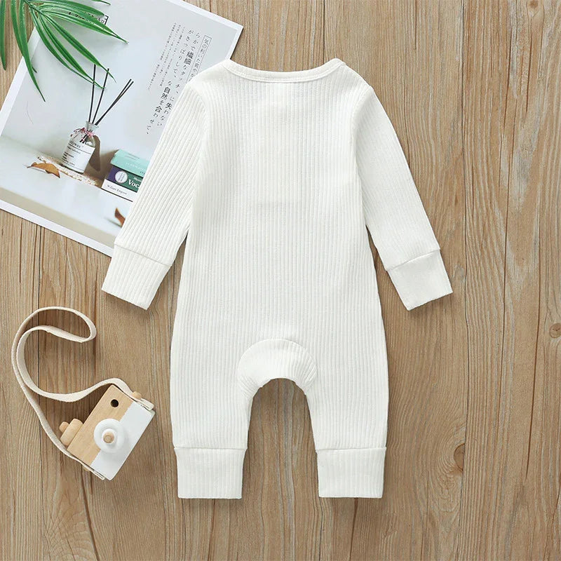 White ribbed cotton baby long sleeve romper on wood background with wooden toy camera and magazine