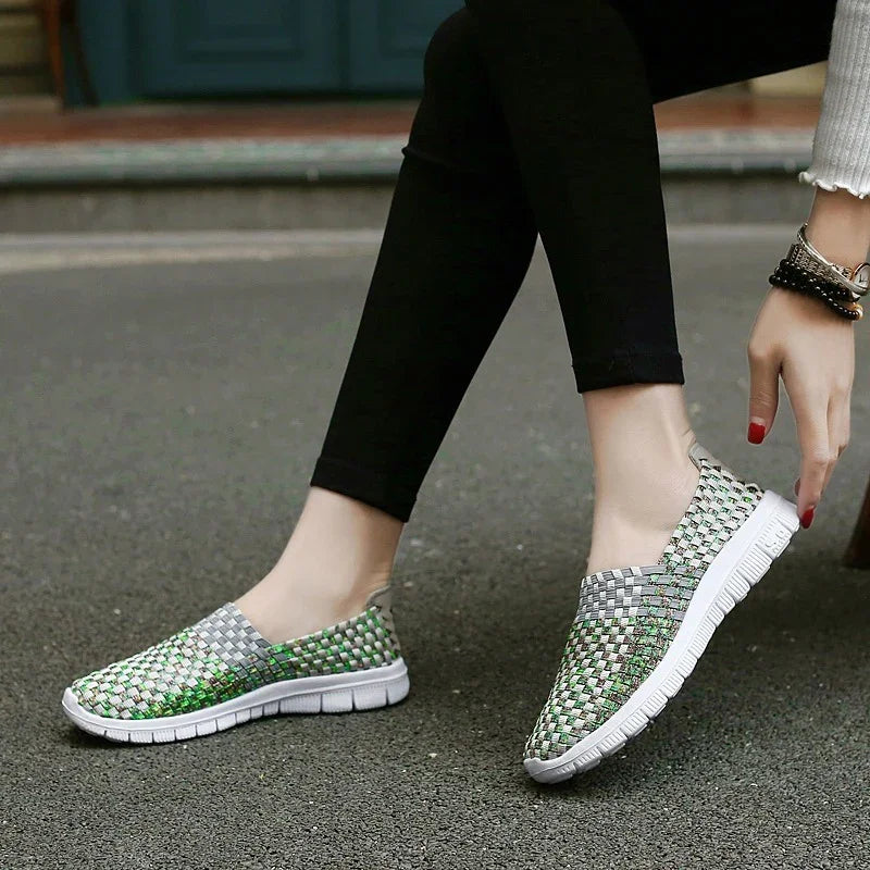 Woman wearing green and gray woven slip-on shoes with white soles and black leggings sitting outdoors