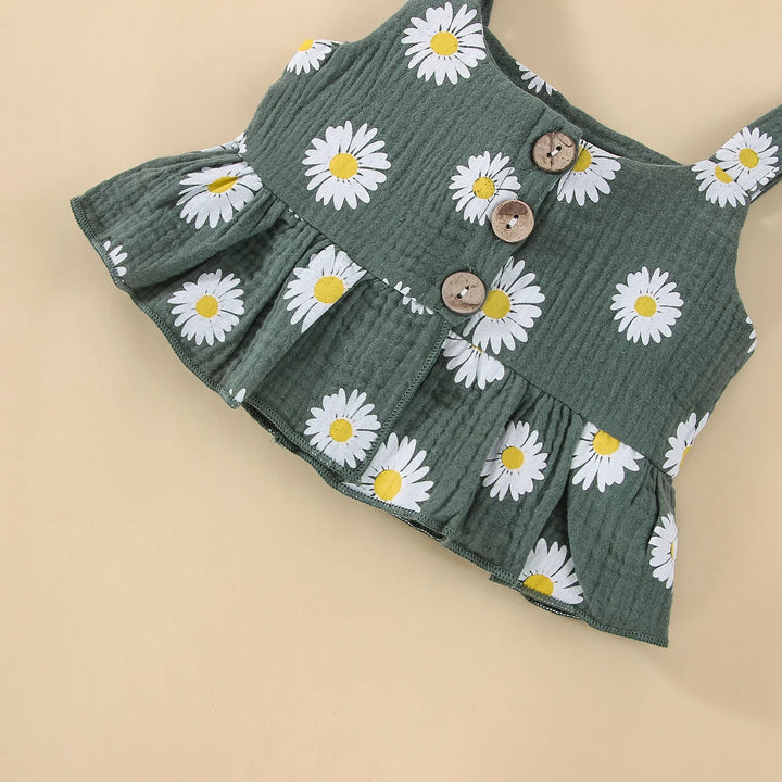Green baby tank top with white daisy print, wooden buttons, and ruffled hem on beige background