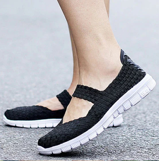 Black woven slip-on casual sneakers with white flexible soles on a person's feet on pavement