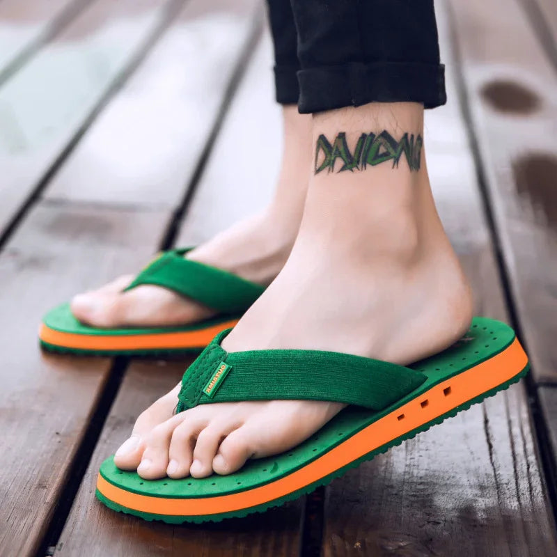 Person wearing green and orange flip-flops on wooden floor with ankle tattoo