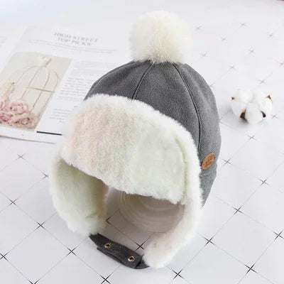 Gray winter trapper hat with white faux fur lining and pom pom on white quilted surface