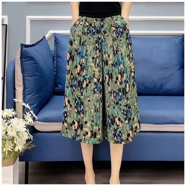 Person wearing abstract print wide-leg culottes standing in front of blue sofa with pillows and white daisies
