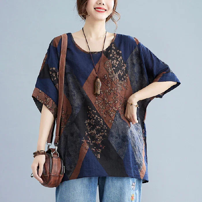Woman wearing loose multicolor geometric floral print top with elbow sleeves, blue jeans, and brown leather crossbody bag