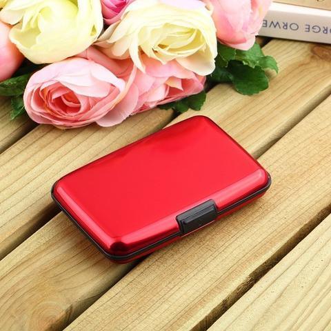 Red metal card holder on wooden surface next to pink and white artificial roses