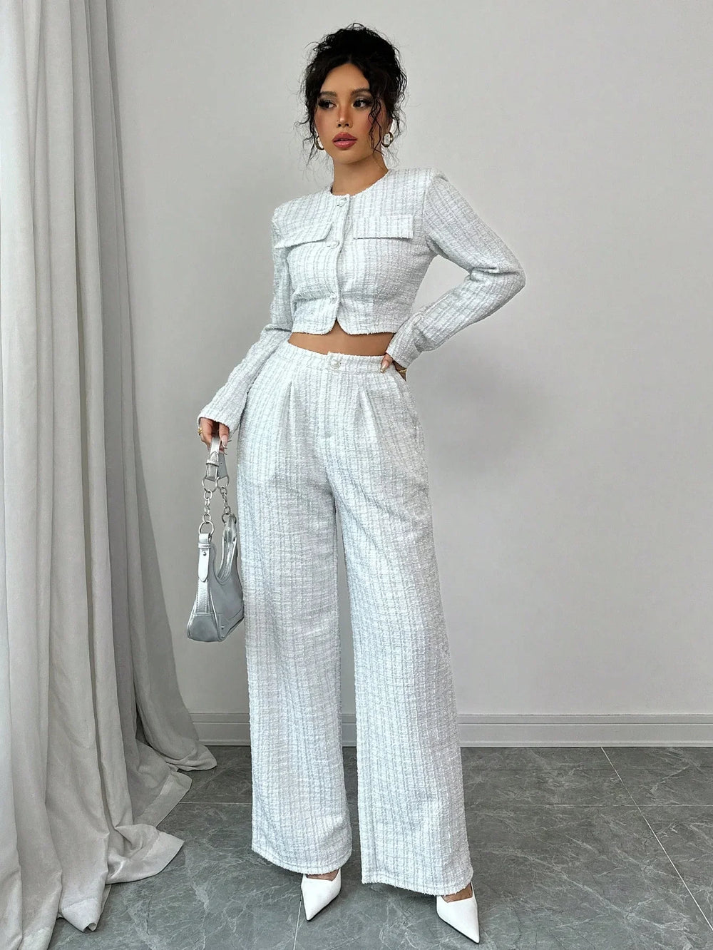 Woman wearing white tweed crop jacket and high-waisted wide-leg trousers with white heels and silver handbag