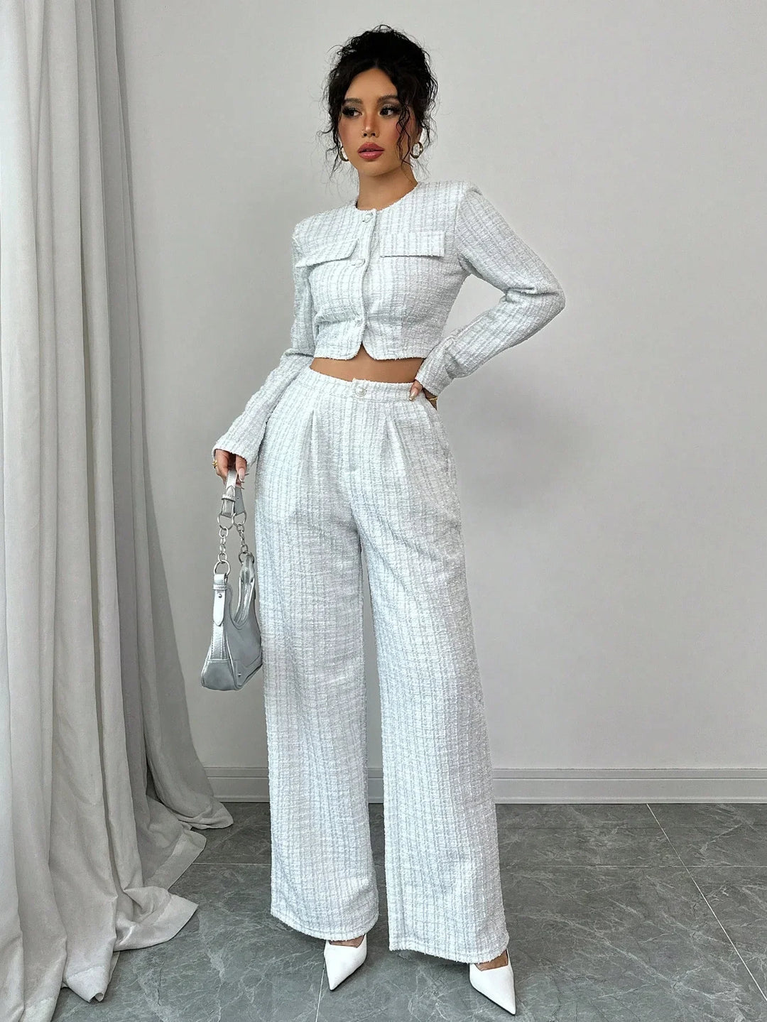 Woman wearing white tweed crop jacket and high-waisted wide-leg trousers with white heels and silver handbag