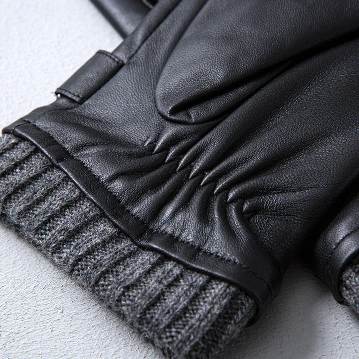 Close-up of black leather gloves with gray knit cuffs on a light surface