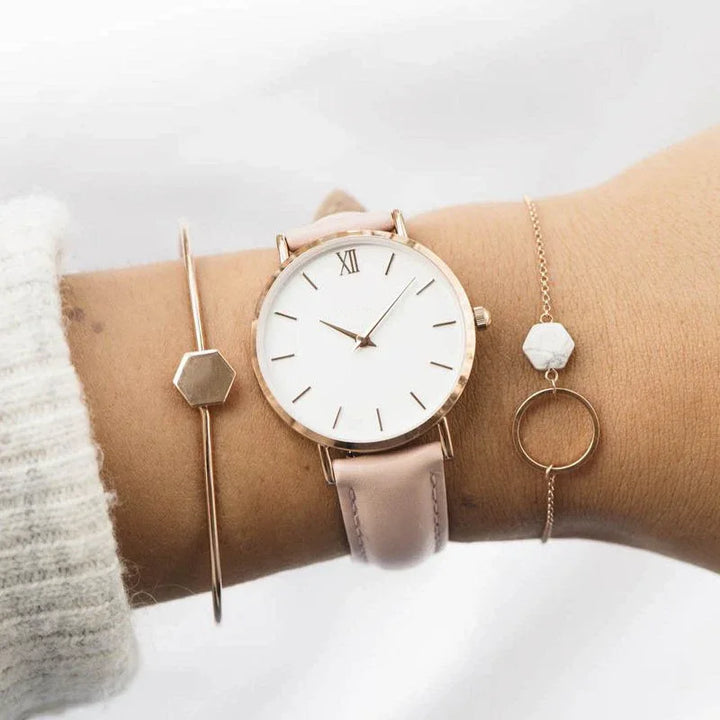 Close-up of wrist wearing a minimalist rose gold watch with light pink leather strap and two delicate bracelets