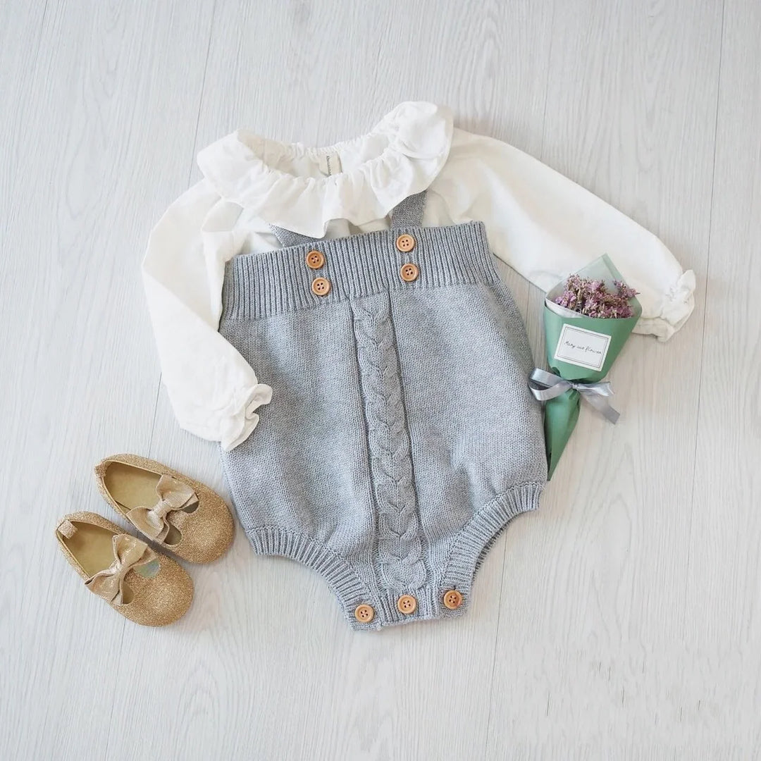 Baby outfit with white ruffled blouse and gray knitted romper with buttons, gold shoes, and small bouquet