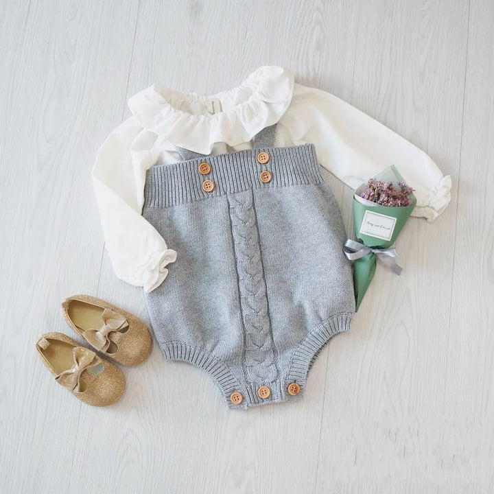 Baby outfit with white ruffled blouse and gray knitted romper with buttons, gold shoes, and small bouquet