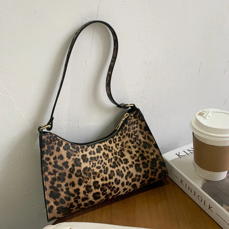 Leopard print shoulder bag with gold zipper on wooden surface beside coffee cup and Kinfolk book