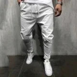 Man wearing white jogger pants and white sneakers standing against a gray wall