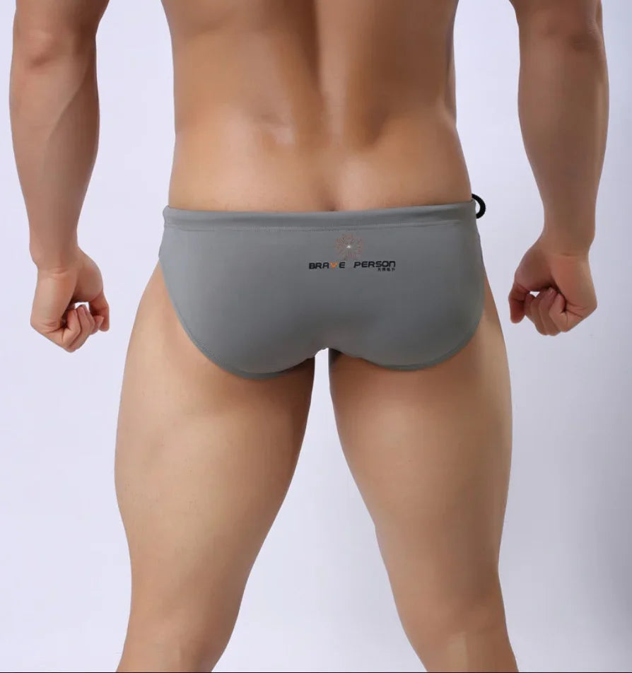Back view of a man wearing gray swim briefs with Brave Person brand logo on a white background