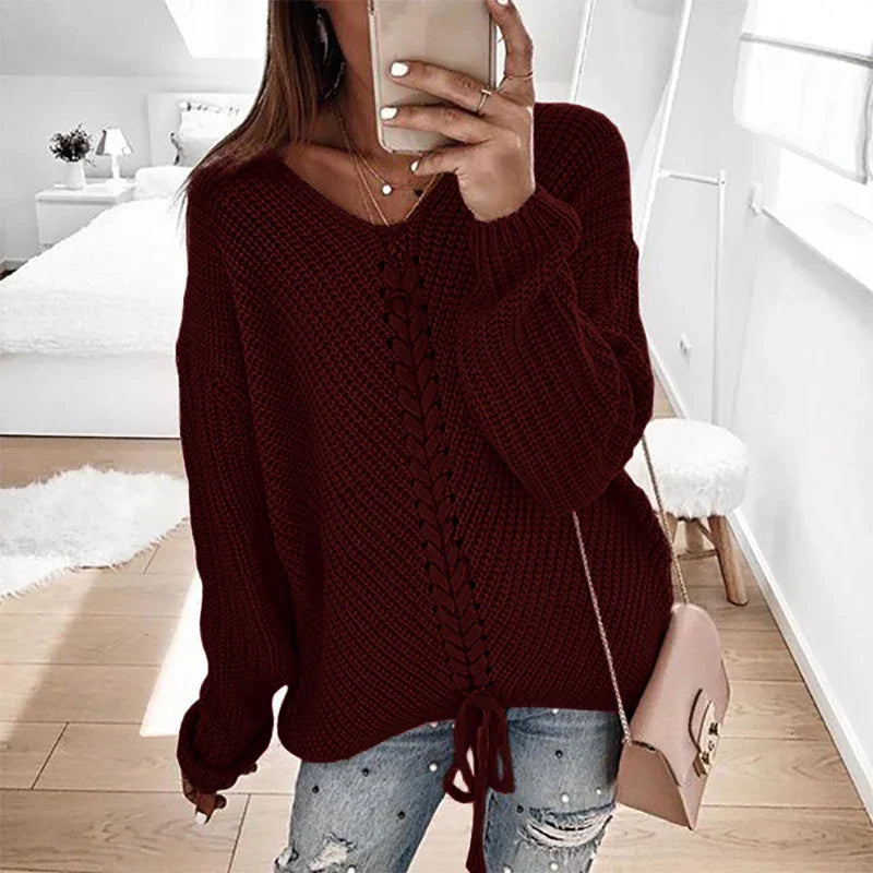 Woman wearing a chunky dark red knit sweater with lace-up front detail and distressed jeans in a bright bedroom