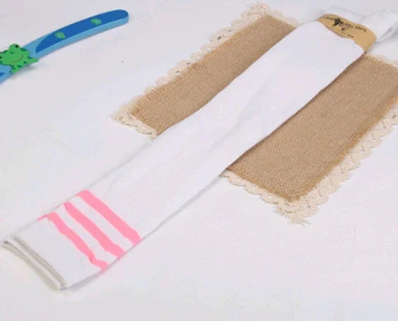 Long white knee-high socks with pink stripes laid on burlap fabric with lace edges