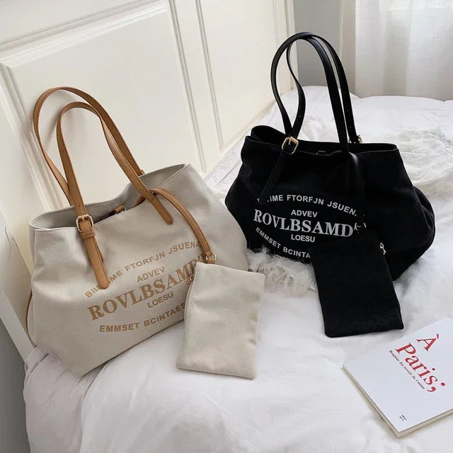 Beige and black canvas tote bags with leather handles and printed text, displayed on a white bed with a book.