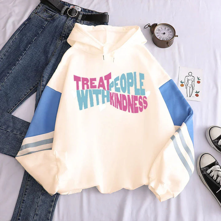White hoodie with blue sleeves and text 'Treat People With Kindness' paired with blue jeans and black sneakers