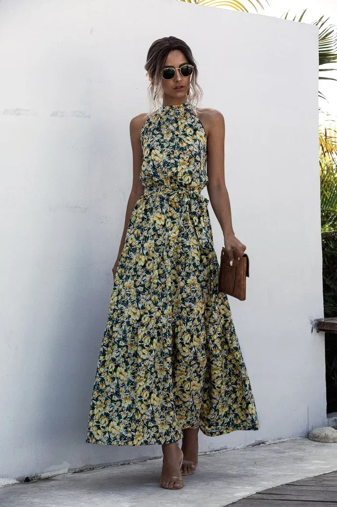 Woman wearing yellow floral halter neck maxi dress with sunglasses holding brown clutch bag