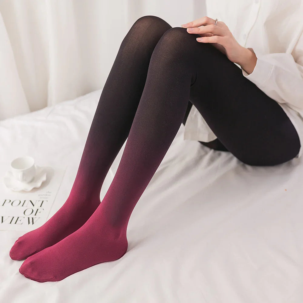 Person wearing black to red ombre gradient tights sitting on white bed with a white cup and magazine