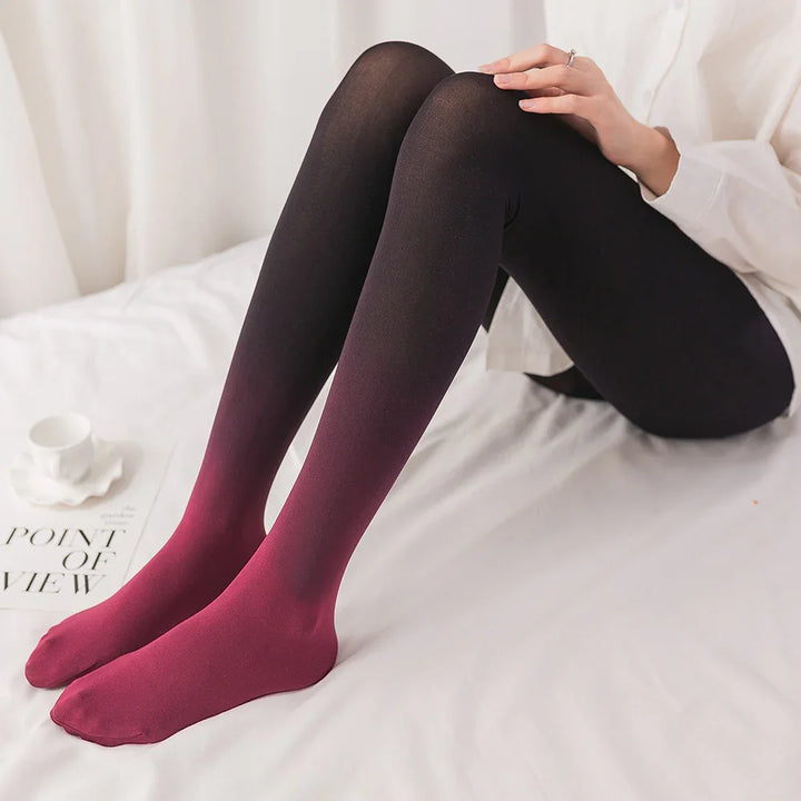 Person wearing black to red ombre gradient tights sitting on white bed with a white cup and magazine