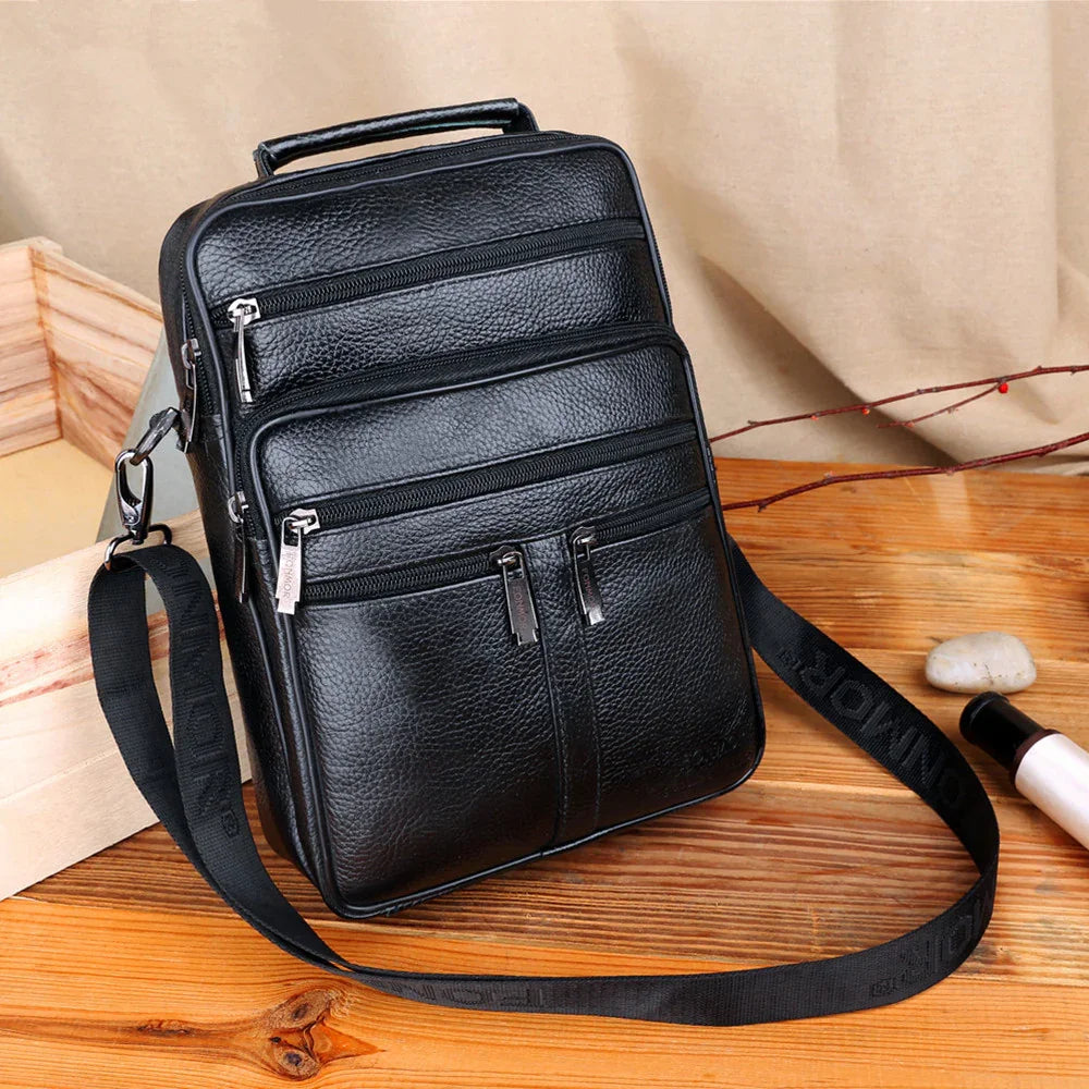 Black leather crossbody bag with multiple zippered compartments on wooden surface