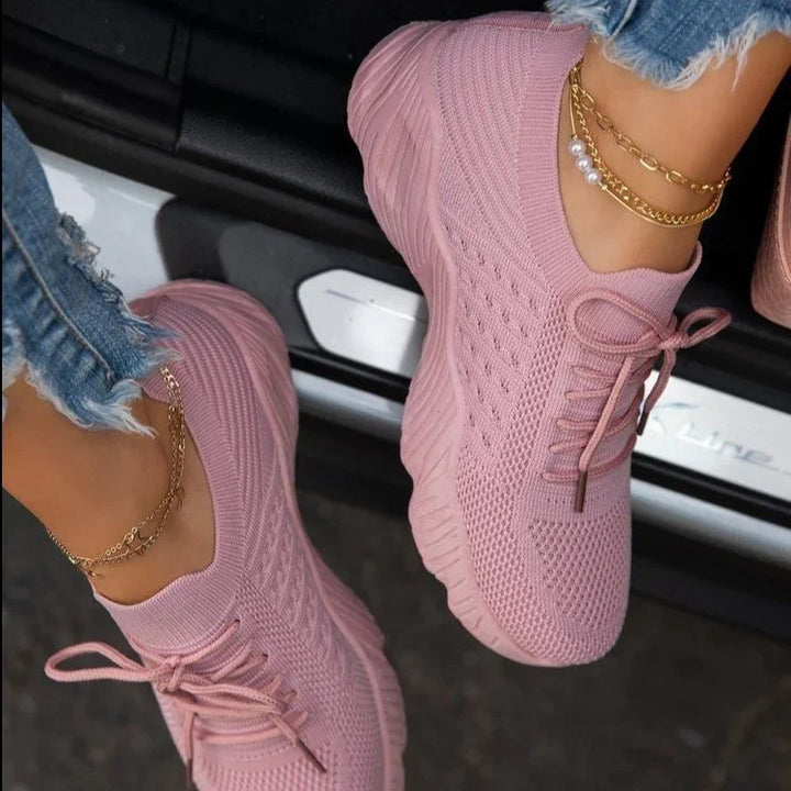 Close-up of feet wearing light pink knit sneakers with frayed blue jeans and gold anklets