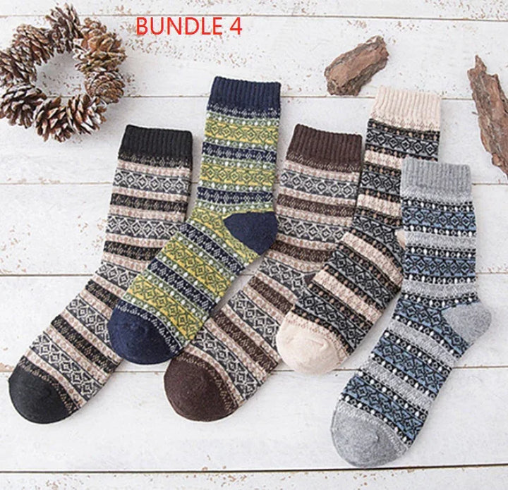 Set of five patterned wool socks in earthy and blue tones displayed on white wooden background with pinecones and bark