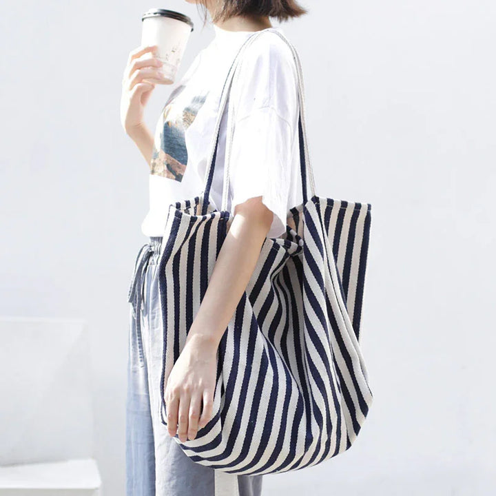 Woman holding striped navy and white tote bag with casual white t-shirt and blue pants, drinking coffee